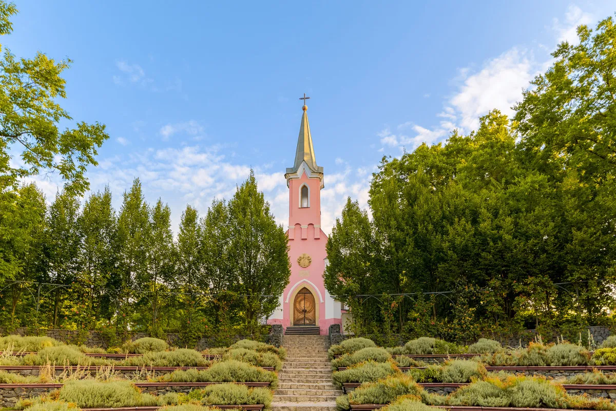 A balatonboglári Vörös kápolna karcsú tornya a fák között emelkedik, a Kápolna-dombról pedig a déli part egyik legpazarabb panorámája látható.